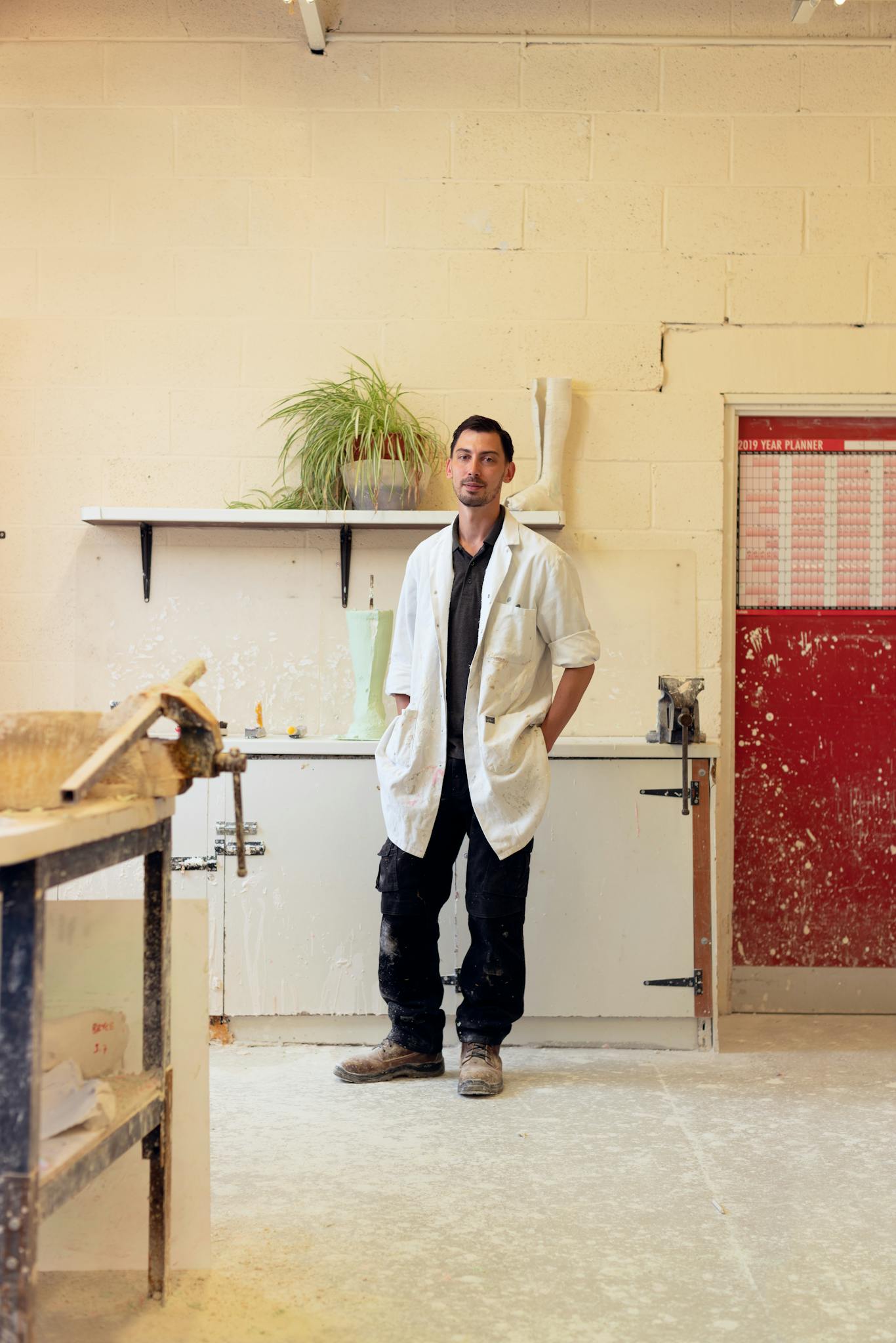 Orthotic technician in workshop wearing a lab coat, surrounded by tools.