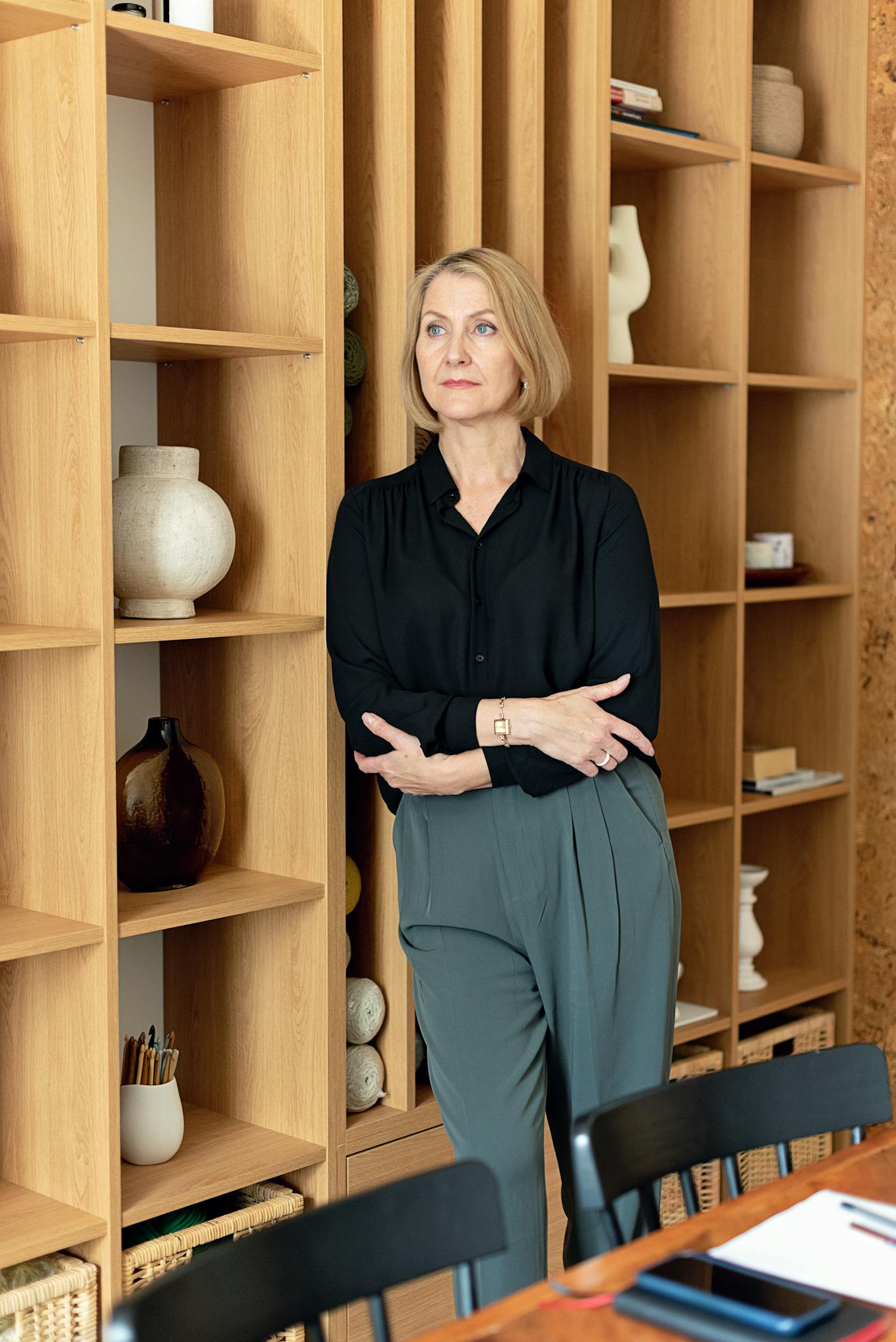 Professional blonde businesswoman in office with shelves. Confident and poised in corporate attire.